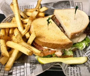 A sandwich and french fries are sitting on a newspaper.