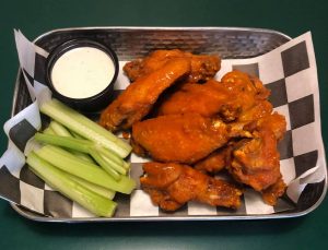 A tray of buffalo wings with celery and dipping sauce.
