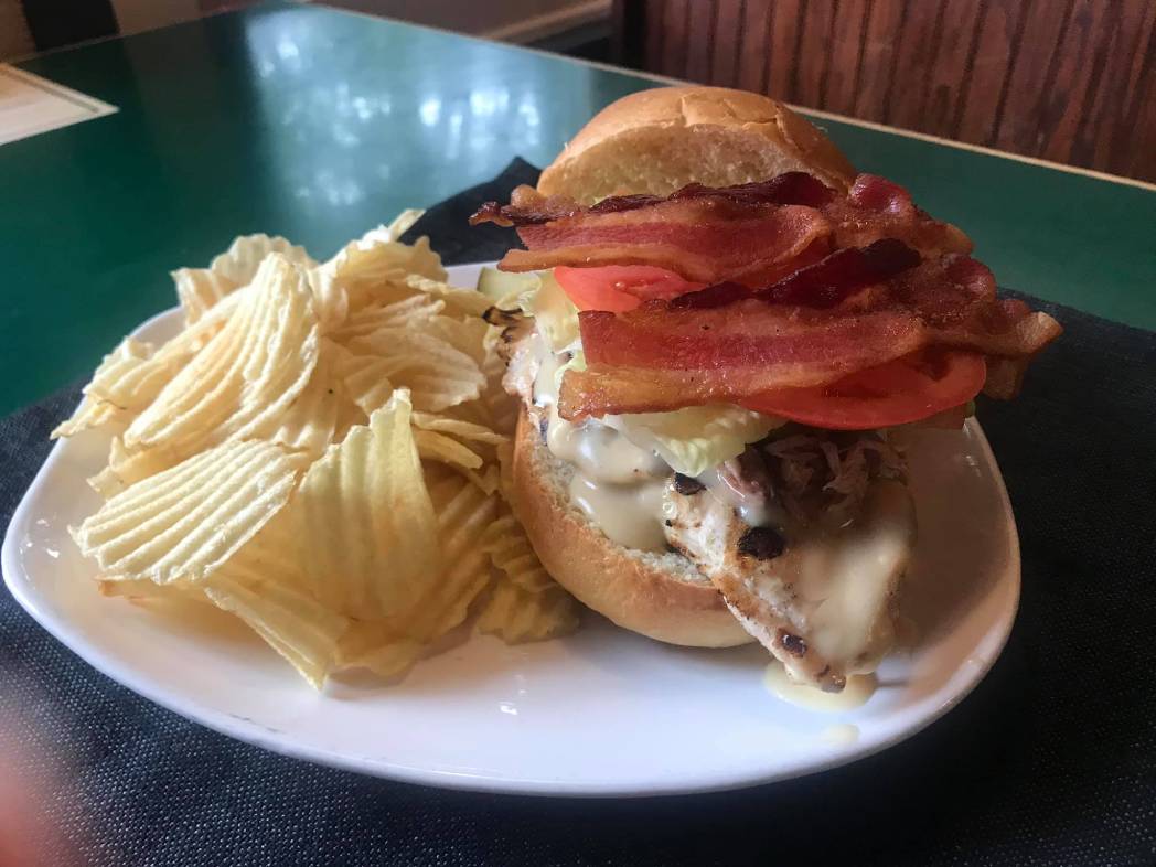 A chicken sandwich with bacon and chips on a plate.